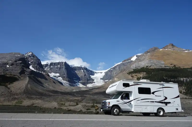 White RV driving in front of mountains with snow.